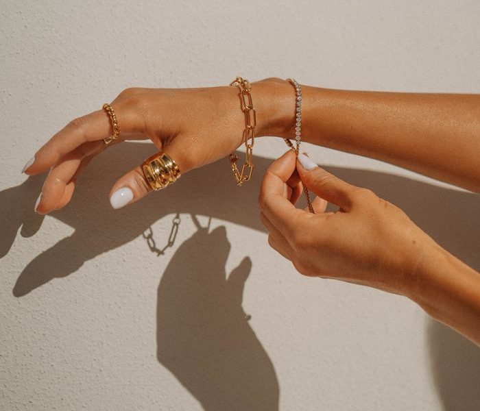 Close-up of hands adorned with gold jewelry casting shadows on a white wall, creating an elegant and artistic composition.