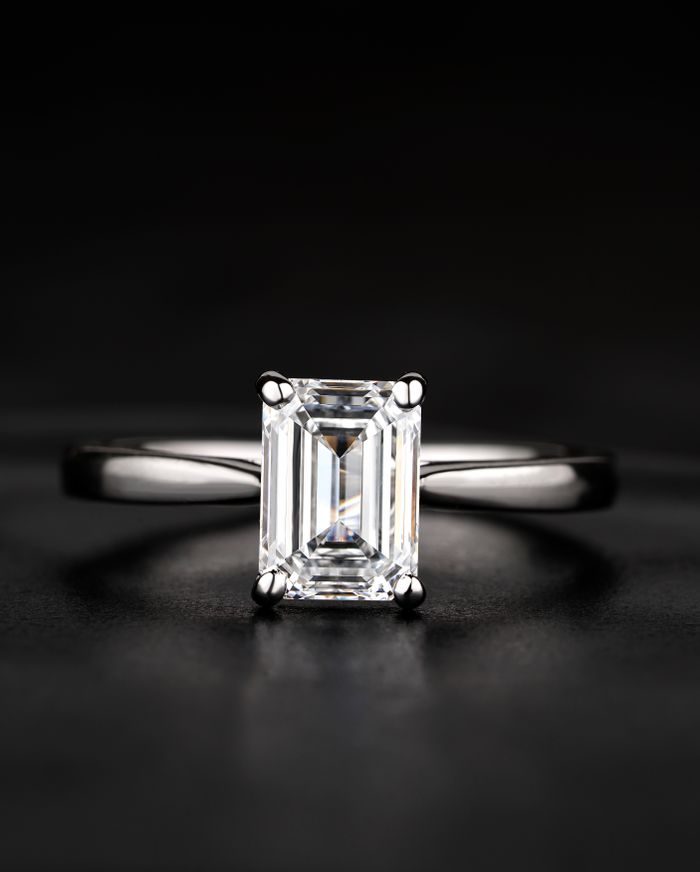 A sparkling emerald cut diamond ring displayed on a luxurious black background, showcasing elegance and sophistication.