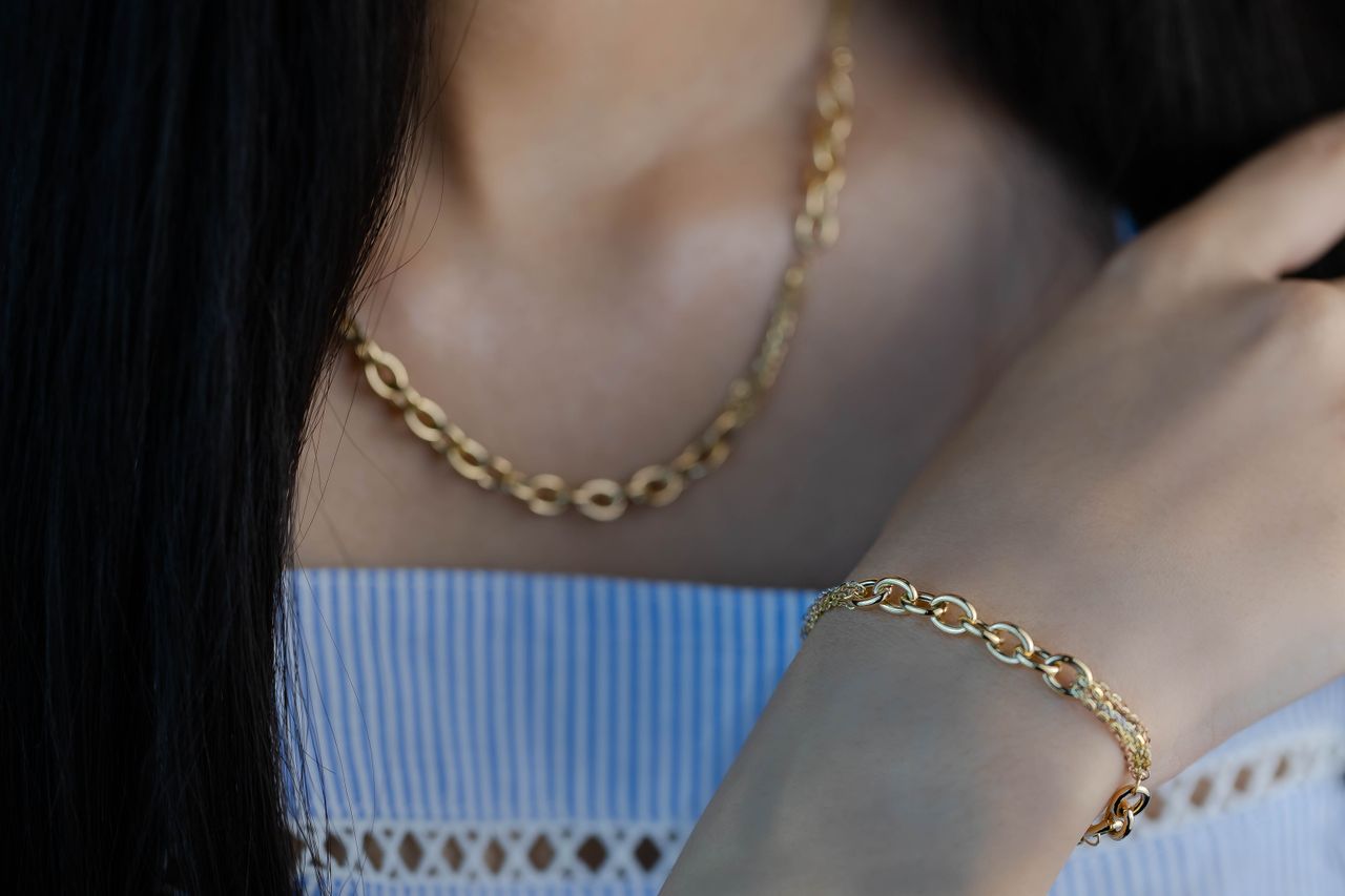 Close-up of a woman wearing gold necklace and bracelet, emphasizing elegance and style.