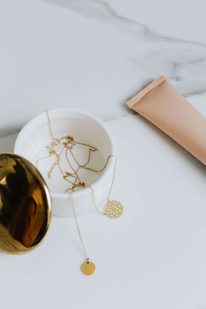 Stylish gold jewelry displayed in a white container with a pink tube on a marble surface, showcasing luxury and elegance.